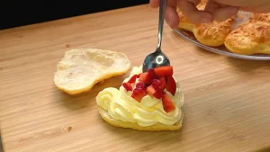 Die untere Hälfte eines gebackenen Herzens wird mit Vanillecreme und Erdbeerstücken belegt
