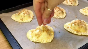 Blätterteigherzen auf dem Blech werden mit Ei bestrichen und mit Haselnüssen bestreut