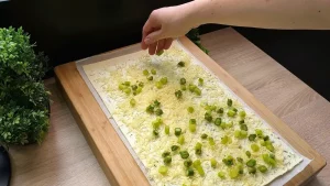 Grüner Spargel und geriebener Käse werden auf dem mit Kräuterfrischkäse bestrichenen Blätterteig verteilt.