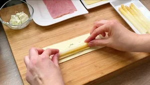 Weißer Spargel wird zusammen mit Schinken und Käse auf Blätterteig-Rechtecke gelegt.