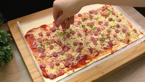 Pizzasauce, Käse, Salami und Frühlingszwiebeln werden gleichmäßig auf den Blätterteig verteilt.