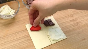 Ein Blätterteig-Quadrat wird in den Vierteln mit Frischkäse, Schokolade und Erdbeeren belegt.