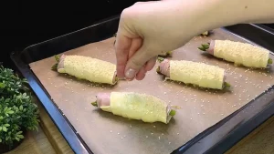 Mit Ei bestrichene Blätterteig-Rollen werden auf dem Blech mit Sesam bestreut.