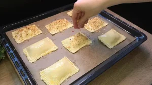 Blätterteig-Taschen auf dem Backblech werden mit Ei bestrichen und mit Haselnüssen bestreut