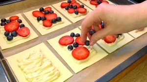 Frische Erdbeerscheiben und Heidelbeeren werden vorsichtig auf die Quarkfüllung gelegt.