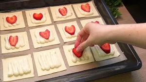 Frische Erdbeerscheiben werden auf die Vanille-Quark-Creme auf dem Blätterteig platziert