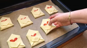Ungebackene Teig-Briefumschläge mit kleinen Teigherzen auf einem Backblech
