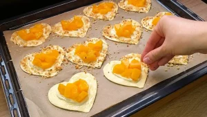 Gehackte Haselnüsse werden auf die mit Ei bestrichenen Ränder der rohen Herzen gestreut