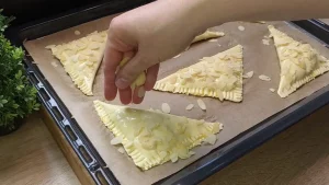 Gehobelte Mandeln werden auf die mit Ei bestrichenen Taschen auf dem Blech gestreut.