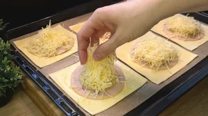 Geriebener Käse wird über die Schinken- und Ananasscheiben auf dem Teig verteilt