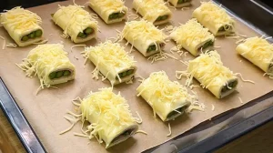 Mit Ei bestrichene Blätterteig-Stücke werden auf dem Backblech mit geriebenem Käse bestreut.