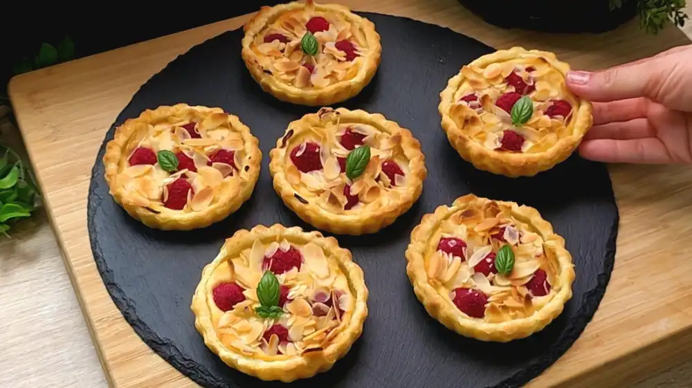 Fertig gebackene Mini-Himbeer-Tartes mit Quarkfüllung und Mandeln.