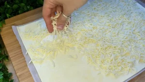 Geriebener Käse wird auf den mit Ei bestrichenen Blätterteig gestreut.