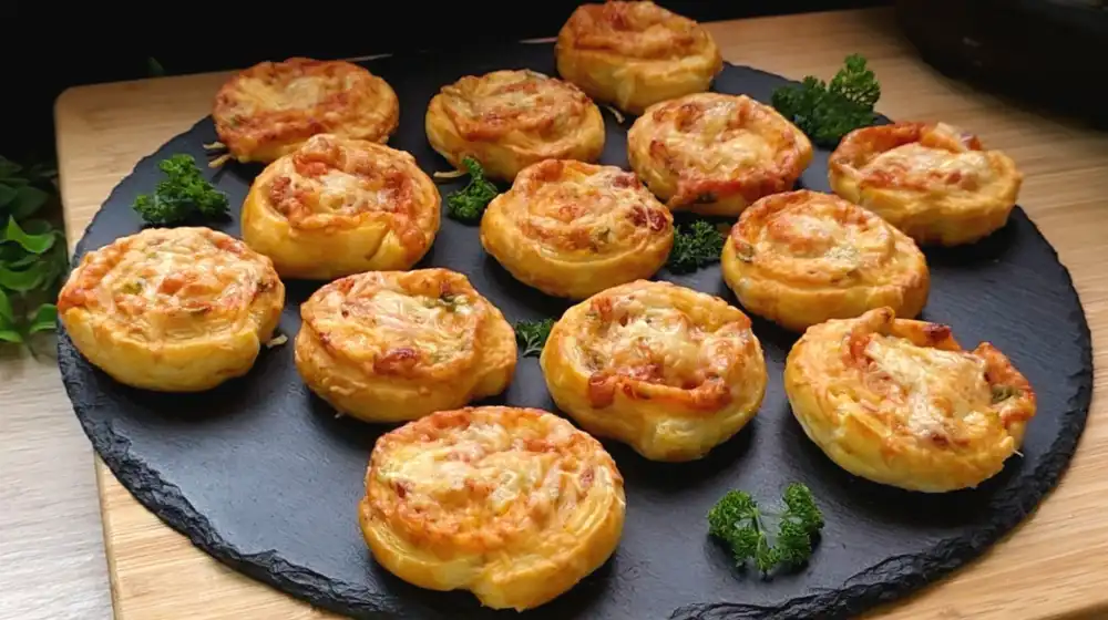 Goldbraun gebackene Pizzaschnecken mit Salami und geschmolzenem Käse auf einer Platte.