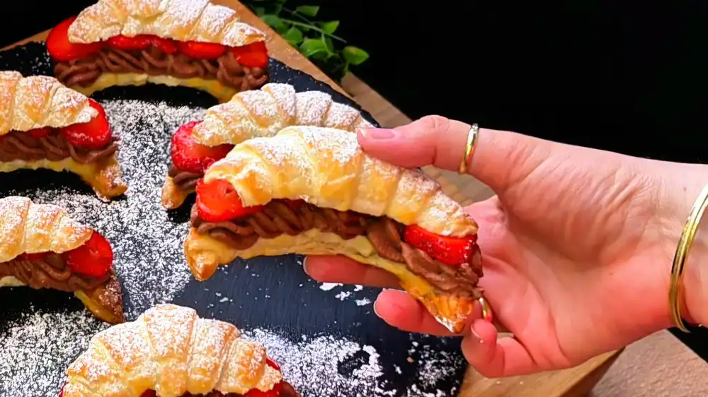 Detailansicht eines aufgeschnittenen Croissants mit üppiger Schokofüllung und Erdbeerscheiben