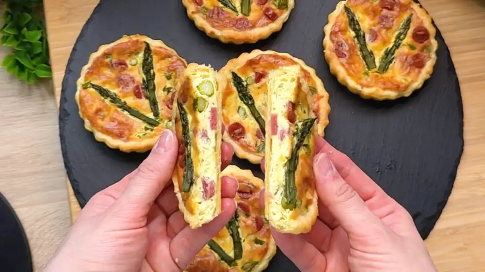 Detailansicht einer Mini-Quiche mit geschmolzenem Käse und sichtbaren Spargelstücken.