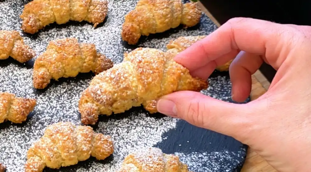 Detailansicht eines Mini-Croissants mit sichtbarer Walnussfüllung und Puderzucker.