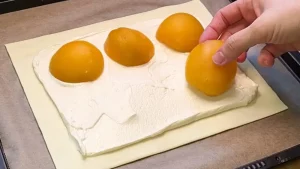 Pfirsichhälften werden auf der Vanille-Quark-Masse auf dem Blätterteig platziert