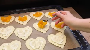 Kleingeschnittene Pfirsiche werden auf die Frischkäse-Schicht auf den Teigherzen gelegt