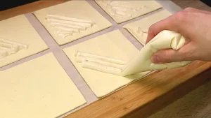 Vanille-Quark-Masse wird auf die vorbereiteten Blätterteig-Quadrate portioniert.