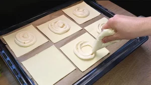 Die Vanille-Quark-Masse wird portionsweise auf die quadratischen Blätterteigstücke gesetzt.