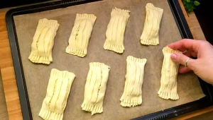 Ungebackene Käsetaschen mit Streifenmuster liegen fertig bestrichen auf dem Backblech