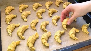 Ungebackene, gerollte Mini-Croissants liegen auf einem Backblech mit Backpapier.