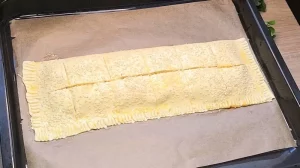 Ungebackener Blätterteig-Snack auf dem Blech, mit Ei bestrichen und Sesam bestreut.
