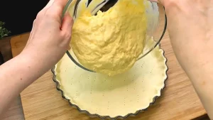 Die cremige Ei-Hollandaise-Mischung wird in die mit Blätterteig ausgekleidete Quicheform gegossen.
