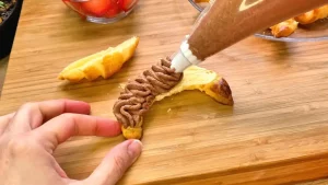 Ein Spritzbeutel füllt die Schokoladen-Sahne-Creme in die halbierten, gebackenen Croissants