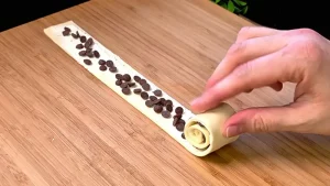 Milchschokoladentropfen werden auf die mit Frischkäse bestrichenen Blätterteigstreifen gestreut