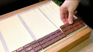 Kleine Schokoladentafeln werden auf die vorbereiteten Blätterteig-Stücke gelegt.