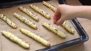 Mit Ei bestrichene Blätterteig-Spargel-Rollen werden mit schwarzem Sesam bestreut.