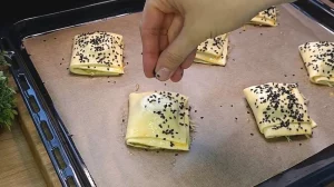 Mit Ei bestrichene Teigtaschen werden vor dem Backen mit schwarzem Sesam bestreut