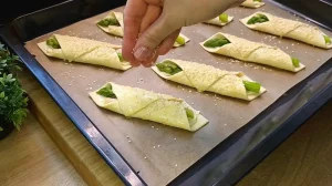 Mit Ei bestrichene Spargel-Taschen werden auf dem Backblech mit Sesam bestreut.