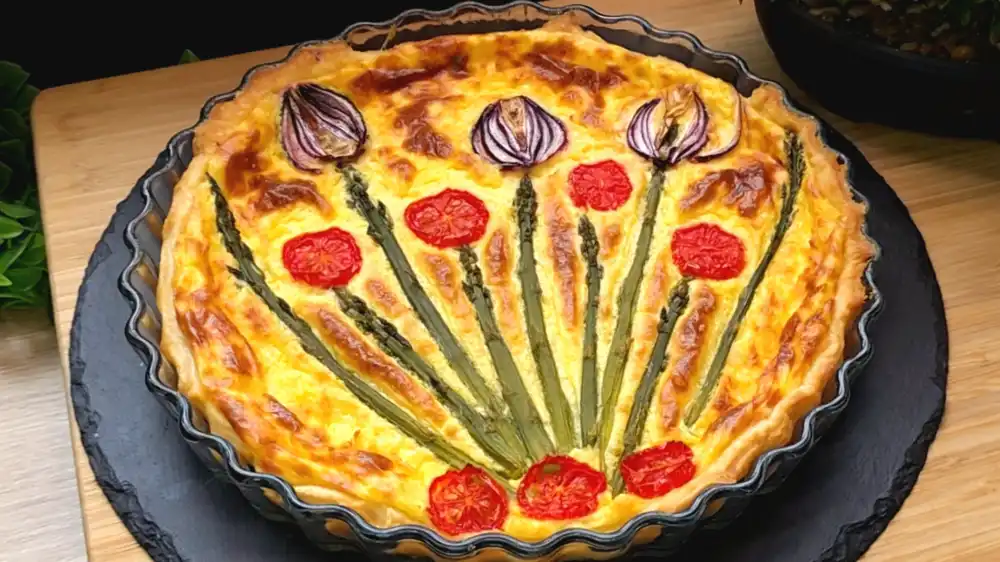 Eine fertig gebackene, goldbraune Blätterteig-Quiche mit grünem Spargel und Cherrytomaten.