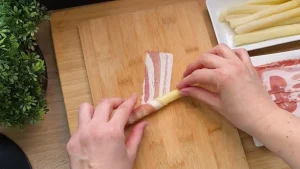 Weißer Spargel wird sorgfältig in eine Scheibe Speck eingerollt.