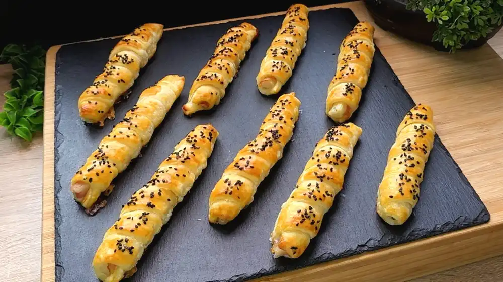 Fertig gebackener weißer Spargel im Blätterteig-Speck-Mantel mit schwarzem Sesam.