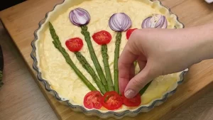 Vorgekochte grüne Spargelstangen, Cherrytomaten und rote Zwiebeln werden kunstvoll auf der Creme platziert.