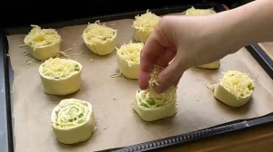 Die geschnittenen Teigschnecken liegen auf dem Backblech und werden mit extra Käse bestreut.