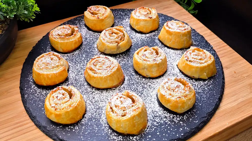 Goldbraun gebackene Blätterteigschnecken mit saftiger Apfel-Zimt-Füllung und feiner Puderzucker-Schneedecke.