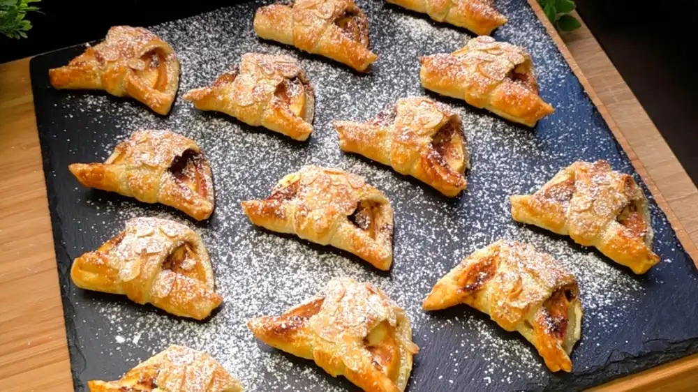 Goldbraun gebackene Blätterteig-Apfeltaschen gefüllt mit Frischkäse und Apfelscheiben, bestreut mit Mandelblättchen.