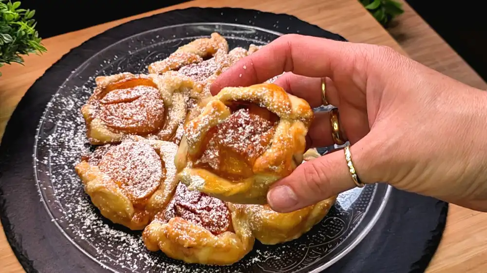 Detailansicht eines einzelnen Segments der Blätterteig-Blume, bei dem das saftige Fruchtfleisch der Aprikose wie ein weichgekochtes Ei aus dem krossen Teig herausschaut.