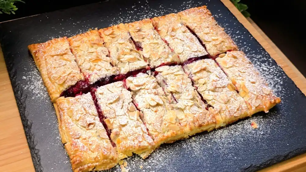 Goldbraun gebackene Blätterteig-Beeren-Vanille-Riegel mit Mandelblättchen und Puderzucker.