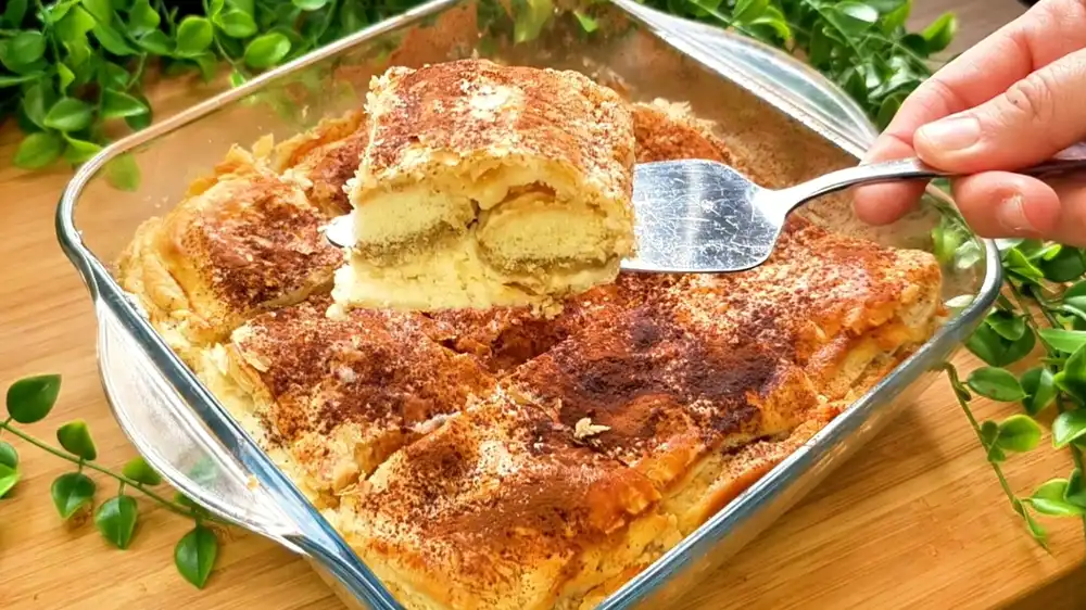 Ein frisch aus dem Kühlschrank servierter Blätterteig Tiramisu Kuchen, dessen krosse Oberseite üppig mit dunklem, ungesüßtem Kakaopulver bestäubt ist.