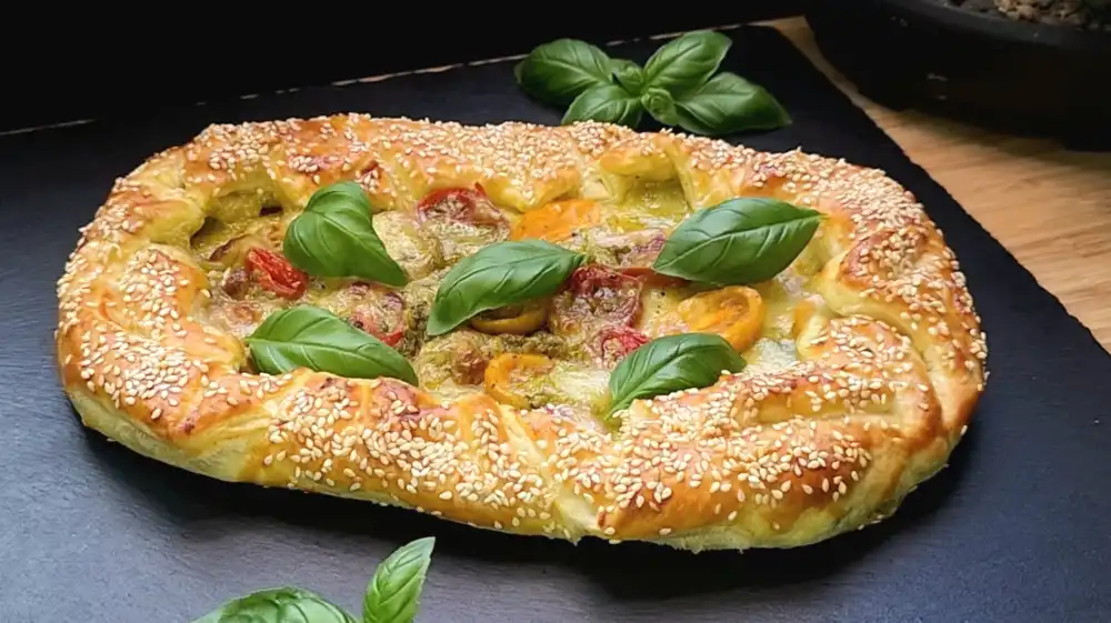 Goldbraun gebackene Blätterteig-Galette mit grünem Pesto, geschmolzenem Mozzarella und Cocktailtomaten.