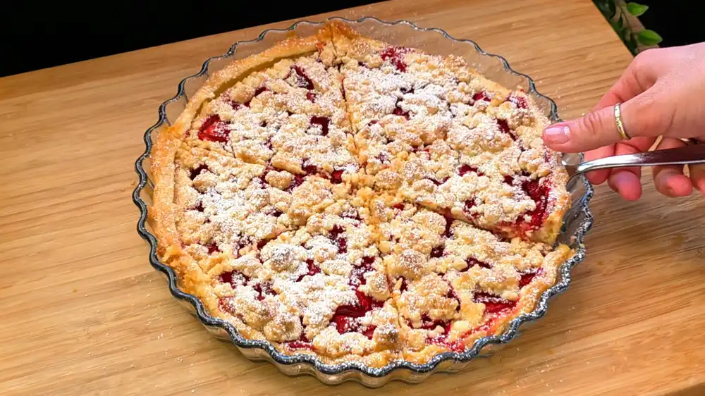Goldbraun gebackener, runder Blätterteig-Kuchen mit einer dicken Schicht aus knusprigen Streuseln, gefüllt mit Quarkcreme und frischen Erdbeerstücken in einer runden Glasform.
