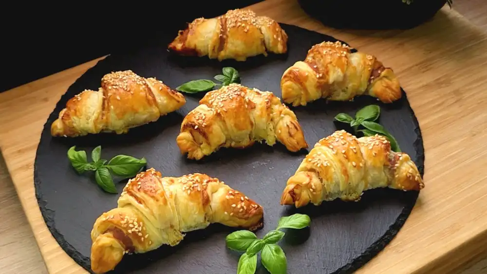 Goldbraun gebackene Blätterteig-Croissants mit Speck und Käse, bestreut mit Sesam auf einer Party-Platte dekoriert mit Fußball-Deko zur WM 2026.