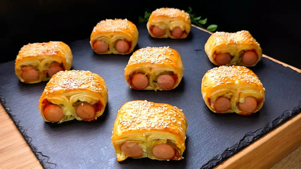 Goldbraun gebackene Hot-Dog-Häppchen aus Blätterteig im Doppelrollen-Look mit geschmolzenem Käse und Sesam.