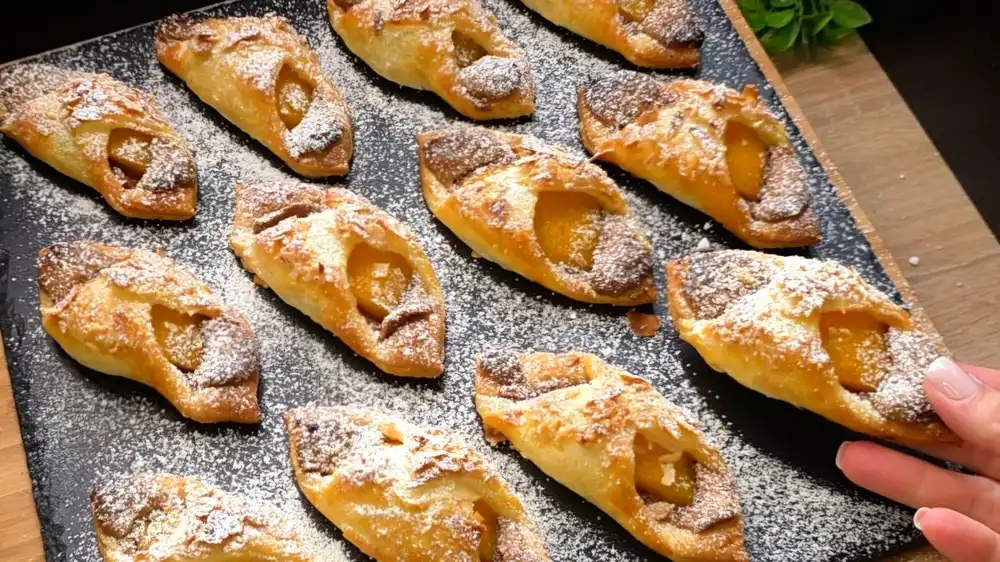 Goldbraun gebackene Blätterteig-Schiffchen gefüllt mit Biscoff-Kekscreme und Pfirsichspalten.